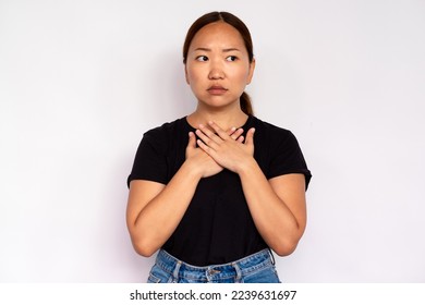 Portrait of uneasy young woman touching her chest over white background. Asian lady wearing black T-shirt and jeans looking away with worried expression. Anxiety concept - Shutterstock ID 2239631697