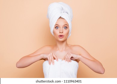 Portrait of unexpected shocked wondered model wrapped in towel with turban on head after shower with big eyes holding towel, afraid of someone, isolated on beige background