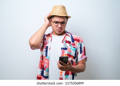 Portrait Of Unhappy Asian Man In Casual Beach Shirt Holding Mobile Phone With Sad Expression On Face While Scratching His Head. Isolated Image On White Background