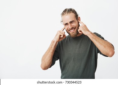 Portrait Of Unhappy Bearded Man Closing Ears With Fingers With Annoyed Expression Trying Not To Hear Bad Singing From Neighbors Apartment.