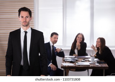 Portrait Of A Unhappy Businessman With His Colleagues Laughing On Him - Powered by Shutterstock