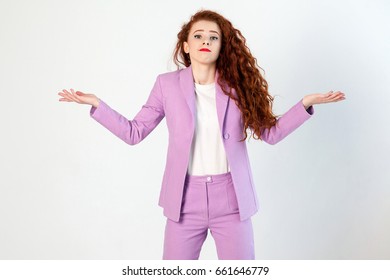 Portrait Of  Unhappy Confused Business Woman With Red - Brown Hair And Makeup In Pink Suit. Looking At Camera, Studio Shot On Gray Background.