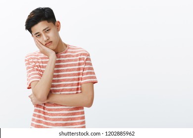 Portrait Of Unhappy Lonely And Sad Young Bored Asian Guy Leaning Head On Palm Looking With Upset Indifferent Gaze At Camera Feeling Uneasy, Feeling Tired Of Boring Lecture Posing Over White Background