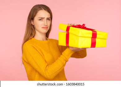 Portrait Of Unhappy Red Hair Girl In Sweater Opening Gift Box And Looking Sadly At Camera, Disappointed With Birthday Surprise, Bad Present And Spoiled Holidays. Indoor Studio Shot Pink Background