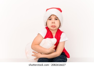 Portrait Of Unhappy Resentful Little Child In Red Santa Claus Hat Isolated On White Background. Beautiful Five-year European Boy. Bad Gift. Copy Space. Merry Christmas. Bad Mood. Close-up. New Year.