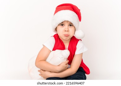 Portrait Of Unhappy Resentful Little Child In Red Santa Claus Hat Isolated On White Background. Beautiful Five-year European Boy. Bad Gift. Copy Space. Merry Christmas. Bad Mood. Close-up. New Year.