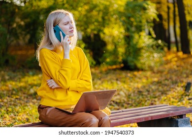 Portrait Of A Unhappy Tired Woman Sitting On The Bench And Talking On The Phone Having Difficult Conversation Outdoors. In Autumn Park.