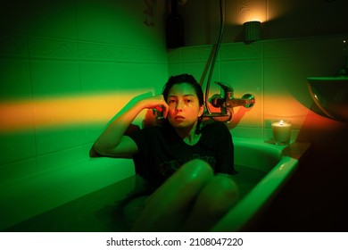 Portrait Of Unhappy Woman Taking Bath Dressed And Tired. Drunk Young Female Lying In Cold Water In Bathroom. Anxious Girl In T-shirt Hiding From Problems. Colorful Neon Light. Midlife Crisis Concept