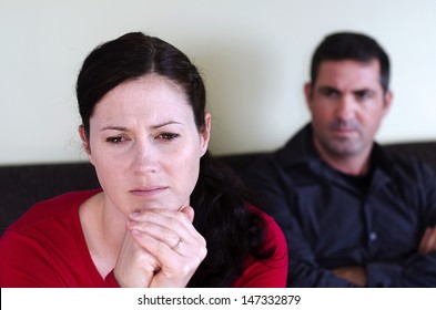 Portrait of unhappy young couple who have fallen out over a disagreement sitting on a sofa. Woman in the front and the man in the background. Real people. Copy space 
