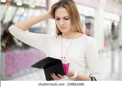 Portrait of unhappy young woman looking in her wallet in shopping center, spent too much, not enough cash, lost money, broke