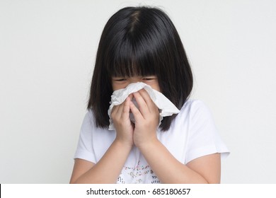 Portrait Of Unhealthy Sick Asia Kid Girl Standing With Napkin Close Her Nose From Allergy Or Rhinitis. Unhappy Ill Child Suffering From Running Nose And Sneezing And Blow Her Nose On White Background