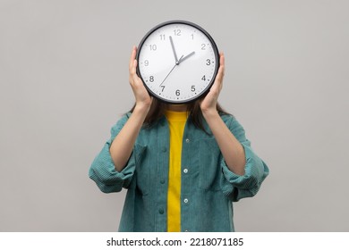 Portrait Of Unknown Woman Holding Wall Clock Hiding Her Face, Time Management, Schedule And Meeting Appointment, Wearing Casual Style Jacket. Indoor Studio Shot Isolated On Gray Background.