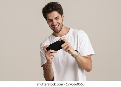 Portrait Of Unshaven Excited Man Playing Online Game On Mobile Phone Isolated Over White Background