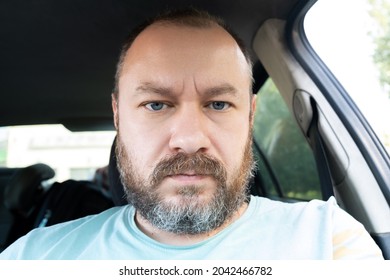 Portrait of an unshaven man 40 years old in a car. An ordinary man frowns at the camera. - Shutterstock ID 2042466782