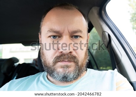 Portrait of an unshaven man 40 years old in a car. An ordinary man frowns at the camera.