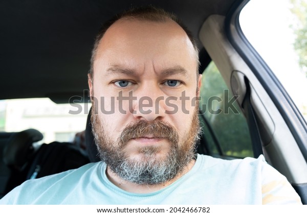 Portrait of an unshaven man 40 years old in a\
car. An ordinary man frowns at the\
camera.