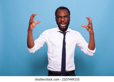 Portrait Of Upset Angry African American Businessman Screaming And Raising Hands On Blue Background. Office Worker Accountant Having A Nervous Breakdown. Frustrated Man Having Aggressive Reaction.