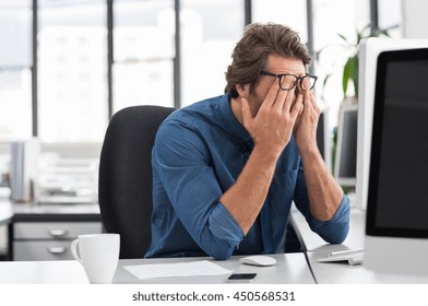 Portrait Of An Upset Businessman At Desk In Office. Businessman Being Depressed By Working In Office. Young Stressed Business Man Feeling Strain In Eyes After Working For Long Hours On Computer.