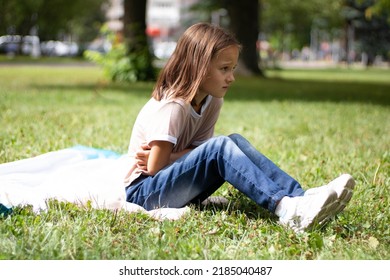 Portrait Of An Upset Frustrated Girl Sitting On The Grass Touching Her Stomach, Suffering From Indigestion, Food Poisoning, Injury, Wearing Denim, Striped Shirts, Covering Her Eyes, Long Curly Wavy Ha