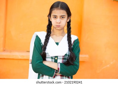 Portrait of upset indian braided hair young girl kid, brunette unhappy asian female standing with arms folded looking at camera over orange background