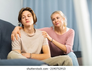 Portrait of upset and offended teenager sitting on sofa while mother soothing him. Mood swings and puberty concept - Shutterstock ID 2190752913