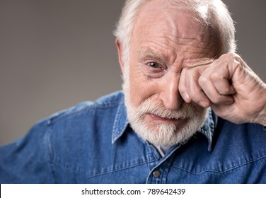 Portrait Of Upset Old Man Rubbing His Eye While Crying. Isolated On Grey Background