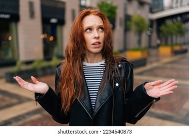 Portrait of upset pretty young woman with long red-hair standing with wet, disheveled hair after being caught in cold autumn rain, sad looking away. Concept of female lifestyle at autumn season.