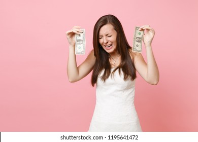 Portrait Of Upset Sad Bride Woman In White Wedding Dress Crying And Holding One Dollar Bills Isolated On Pastel Pink Background. Lack Of Money. Organization Of Wedding Celebration Concept. Copy Space