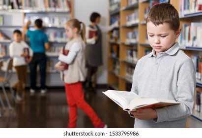 Portrait Of Upset Tween Boy Browsing Book In School Library

