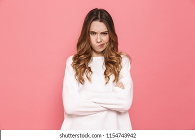 Portrait of an upset young casual girl standing with arms folded isolated over pink background