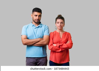 Portrait of upset young couple in casual wear standing together with crossed hands, looking sideways at each other with resentful glance, suspicion. isolated on gray background, indoor studio shot