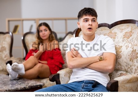 Portrait of upset young man sitting while quarrel with wife at home interior