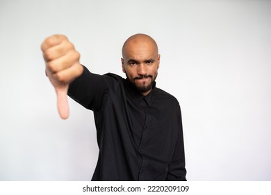 Portrait Of Upset Young Man With Thumb Down. Dissatisfied Multiethnic Male Model With Bald Head And Beard In Black Shirt Looking At Camera, Disapproving Idea. Dislike Concept