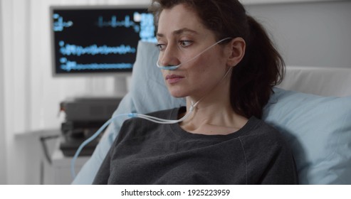 Portrait Of Upset Young Woman Patient With Nasal Cannula Delivering Oxygen Resting In Bed At Hospital. Sick Female With Breathing Tube Feeling Upset And Stressed Lying In Hospital Ward