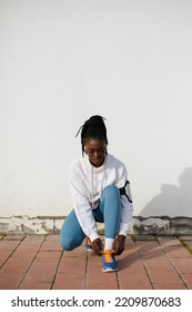 Portrait Of Urban Female Runner Getting Ready For Training Outside. Sporty Young Black Woman Looking At Camera While Lacing Her Running Shoes. Fitness Lifestyle And Motivation.