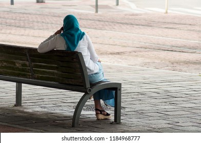 Portrait Of Veiled Muslim Woman Sitting On Bench With Phone On Back View