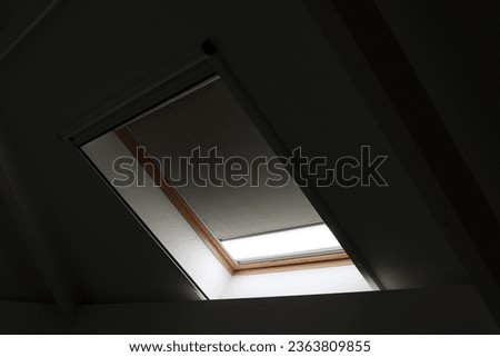 A portrait of a velux skylight window almost closed by a blinding. The blind is making the room dark, but still lets some light enter. This also keeps warmth outside and keeps it cool inside.