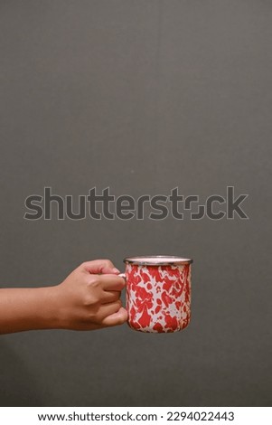 Portrait or vertical shot of a handheld vintage enamel mug on a dark grey background