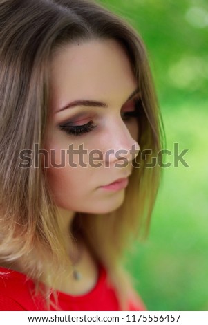 Portrait of a very beautiful girl in a red dress in green leaves of a tree.