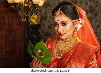 Portrait Of Very Beautiful Indian Bride Holding Betel Leaf, Bengali Bride In Traditional Wedding Saree With Makeup And Heavy Jewellery In Studio Lighting Indoor