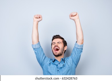 Portrait of very excited young man, celebrating victory with raised hands and screaming