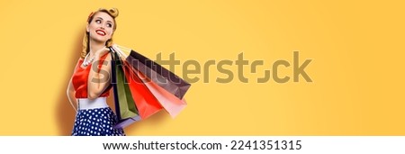 Portrait of very happy, cheerful excited looking up woman in pinup dress holding, carrying many shopping bags, isolated on yellow color background. Sales discounts rebates or consumer bank credit ad.