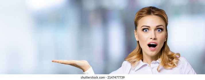 Portrait of very happy, excited surprised, astonished businesswoman with wide opened eyes, mouth, showing something or copy space area. Success in business concept. Blurred office background.
