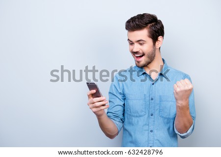 Portrait of very happy hansome brunet reading a message on his pda and celebrating victory