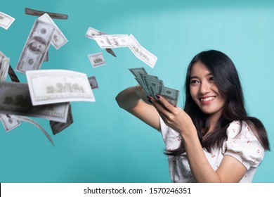 Portrait of very happy  young asian woman throwing out money banknotes on cyan color background