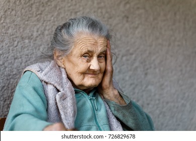 Portrait Of A Very Old And Tired Of Life Wrinkled Woman Outdoors With A Hand Near Her Face