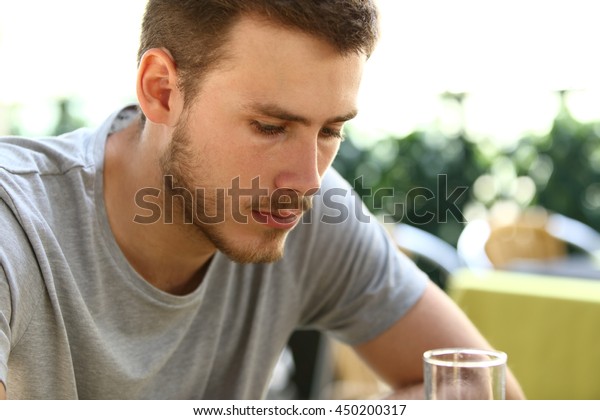 Portrait of a very sad single man\
sitting alone and drinking outside in a restaurant\
terrace