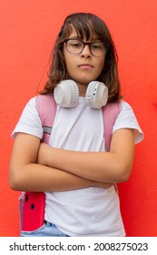Portrait of a very serious schoolgirl in front of a red wall of the school. Back to school concept