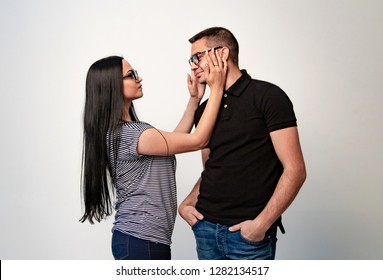 Portrait View Of Beautiful Couple In Eyeglasses Looking At Each Other With Love While Standing In Studio. Dressed In T-shirts And Jeans Girl And Her Boyfriend Wearing Glasses.