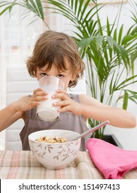 Portrait view of a child boy sitting at home by a breakfast table drinking milk from a glass with cereals in his food bowl, interior.
